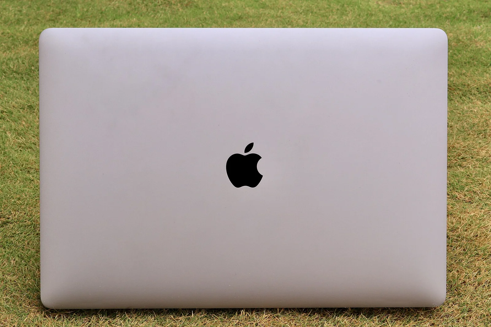 잔디가 깔린 야외 배경 위에 덮개가 열린 상태로 놓인 Apple MacBook Pro 노트북 사진.