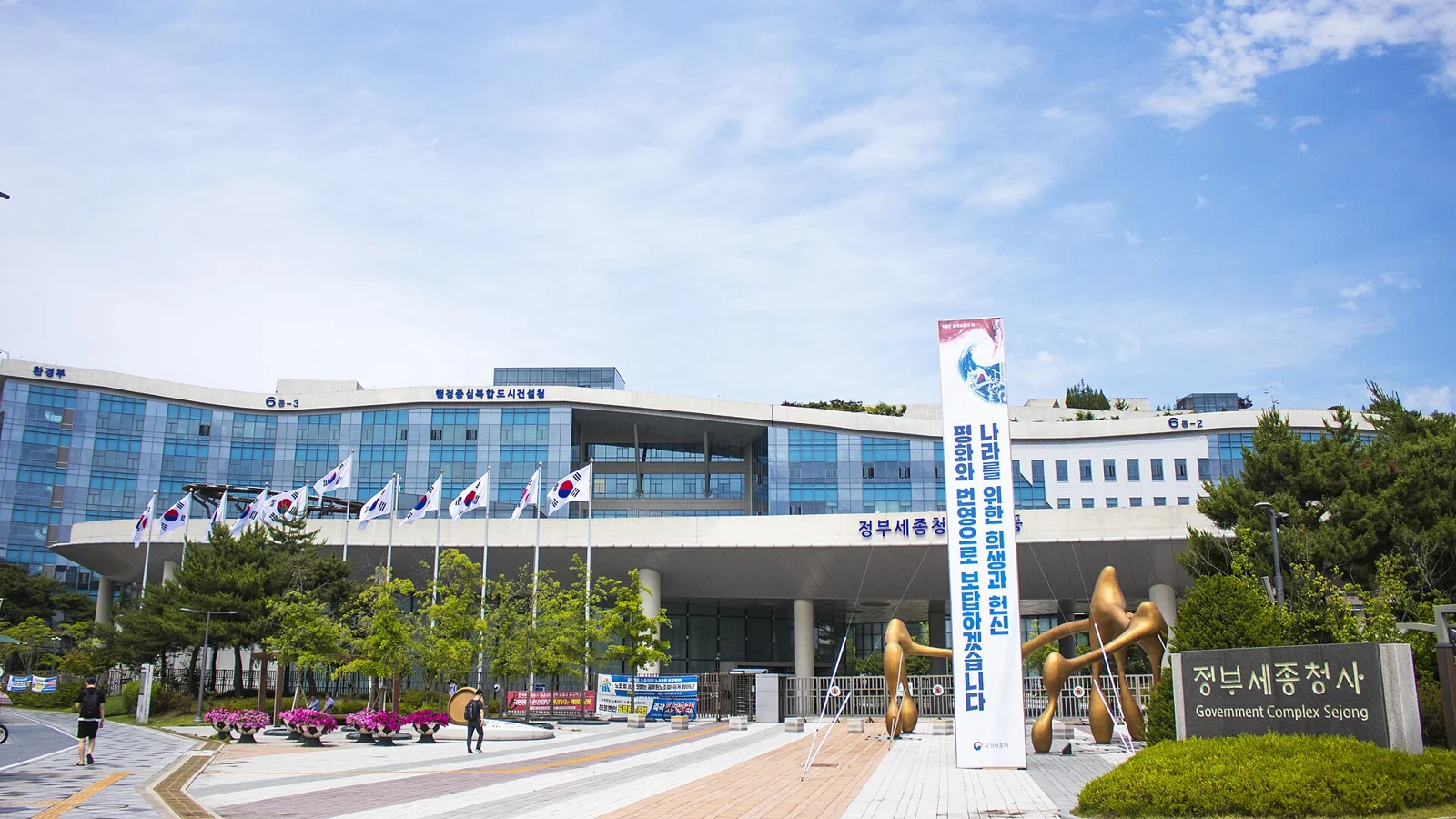세종특별자치시에 있는 정부세종청사의 모습. 여러 층의 흰색 계열 건물 앞으로 정문과 안내소가 보인다.