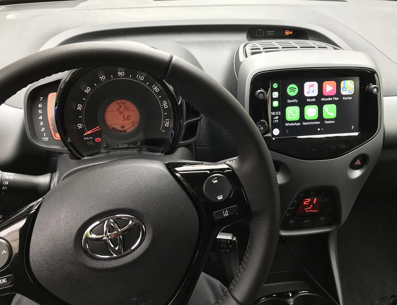 토요타 아이고 차량 내부 센터 디스플레이에 Apple CarPlay 인터페이스가 표시된 모습. 차량 계기판 아래 화면에 앱 아이콘과 지도 메뉴가 보인다.