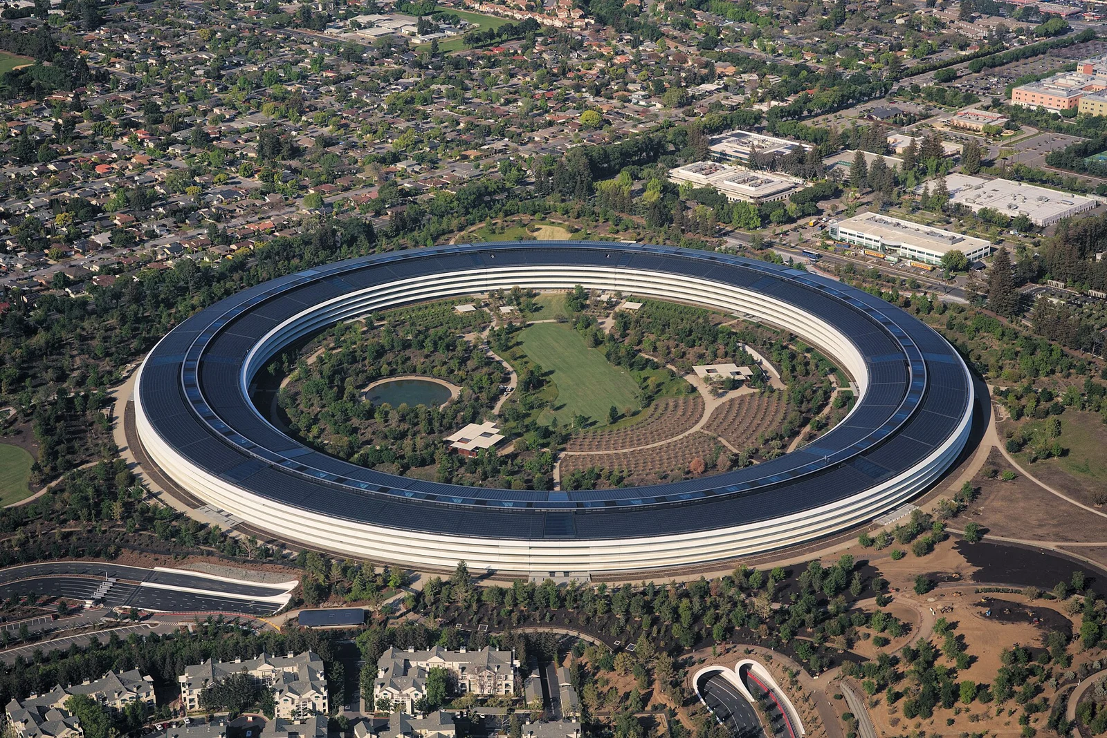 캘리포니아 쿠퍼티노에 있는 Apple Park 본사 건물을 위에서 내려다본 항공 사진이다. 원형에 가까운 건물 지붕 전체가 태양광 패널로 덮여 있다.