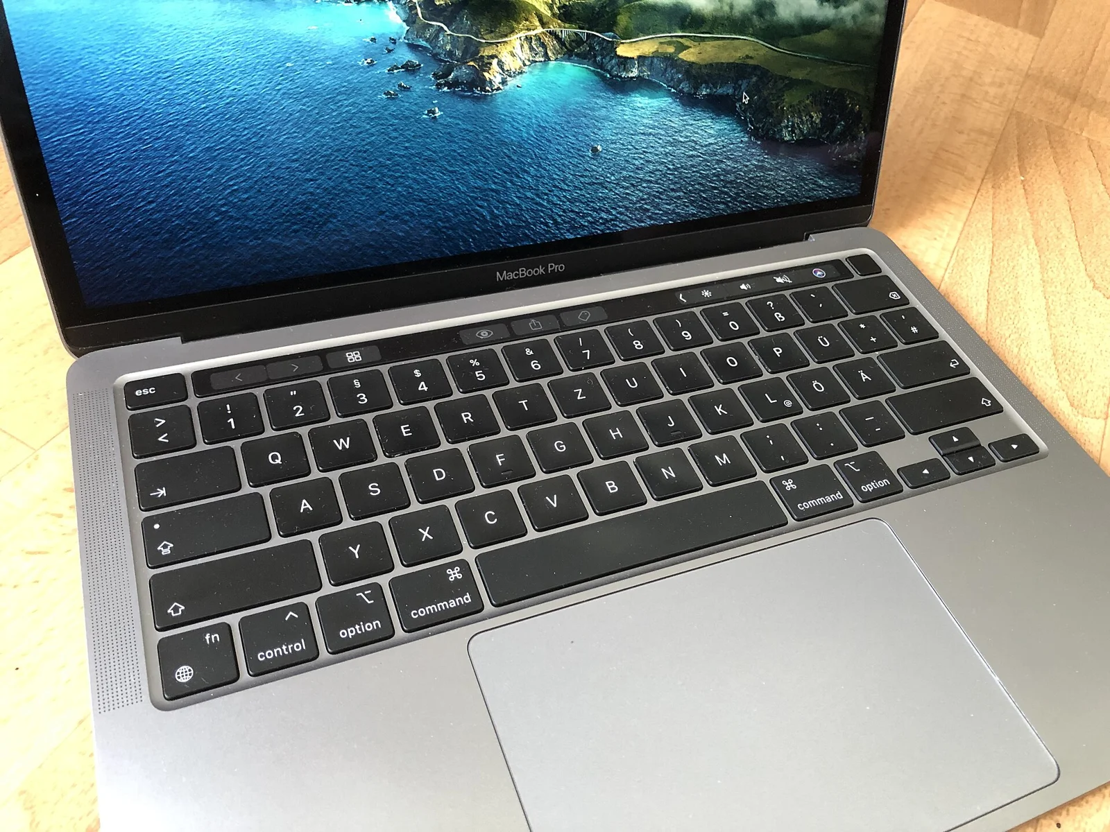 회색 금속 케이스의 MacBook Pro 13인치 노트북이 열린 상태로, 키보드 위쪽에 터치바가 보인다.